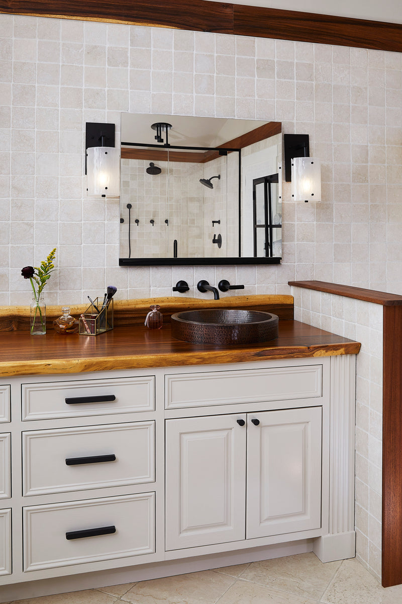 Bathroom with wooden vanity, white cabinets, and tiled walls.