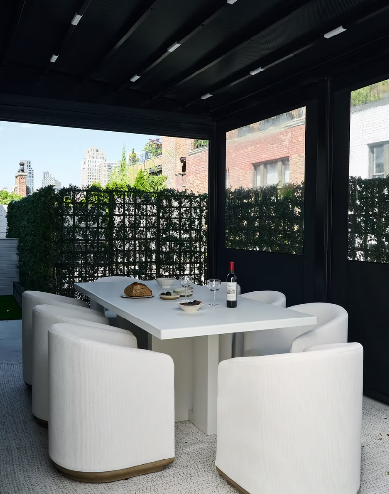 Modern outdoor dining area with white table and chairs, cityscape in the background.