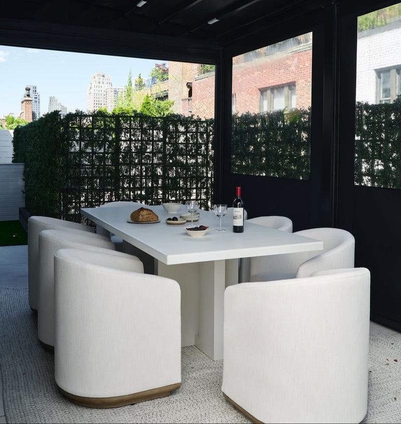 Modern outdoor dining area with white table and chairs on a rooftop with cityscape view.