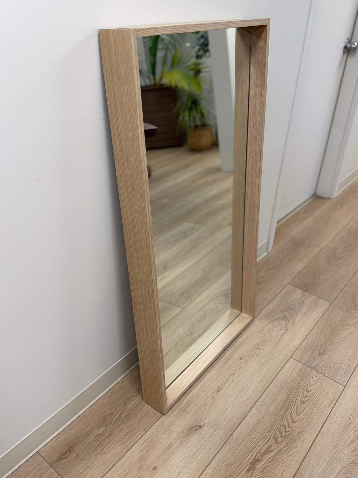 Wooden-framed mirror leaning against a white wall on a wooden floor.