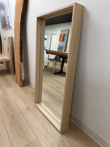 Wooden floor mirror leaning against a wall in a room with furniture.